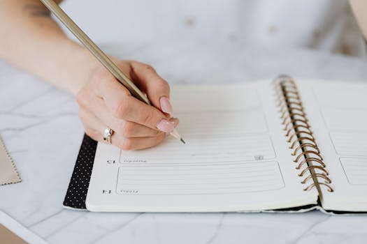 Close-up of a woman's hand writing in a spiral notebook on a marble desk.